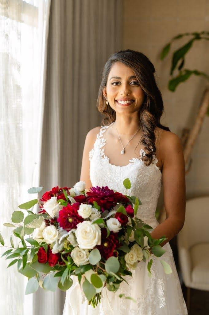 Bride in white lace gown holding red and white floral bouquet