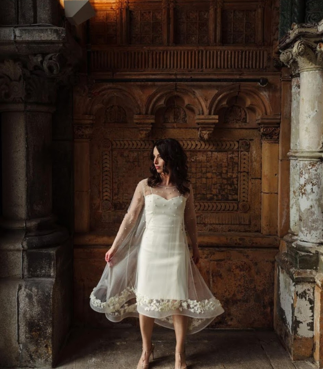 Bride in short white gown with floral tulle cape in ornate stone hallway