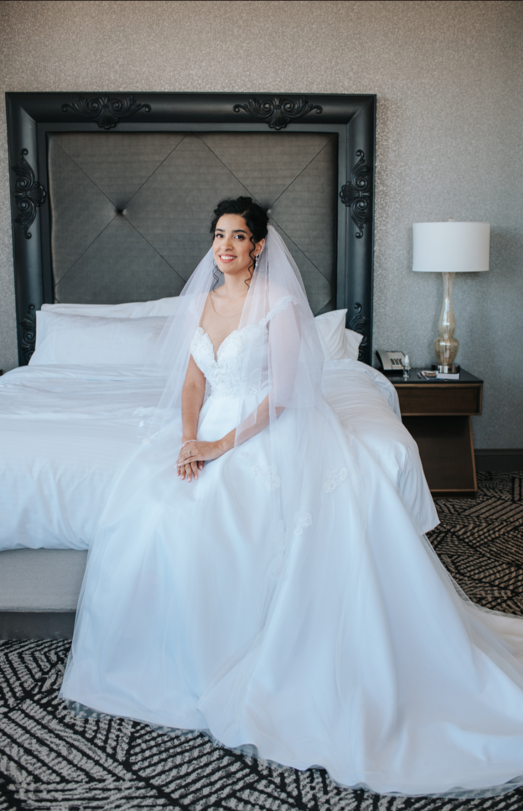 Bride in ballgown with veil seated on hotel bed