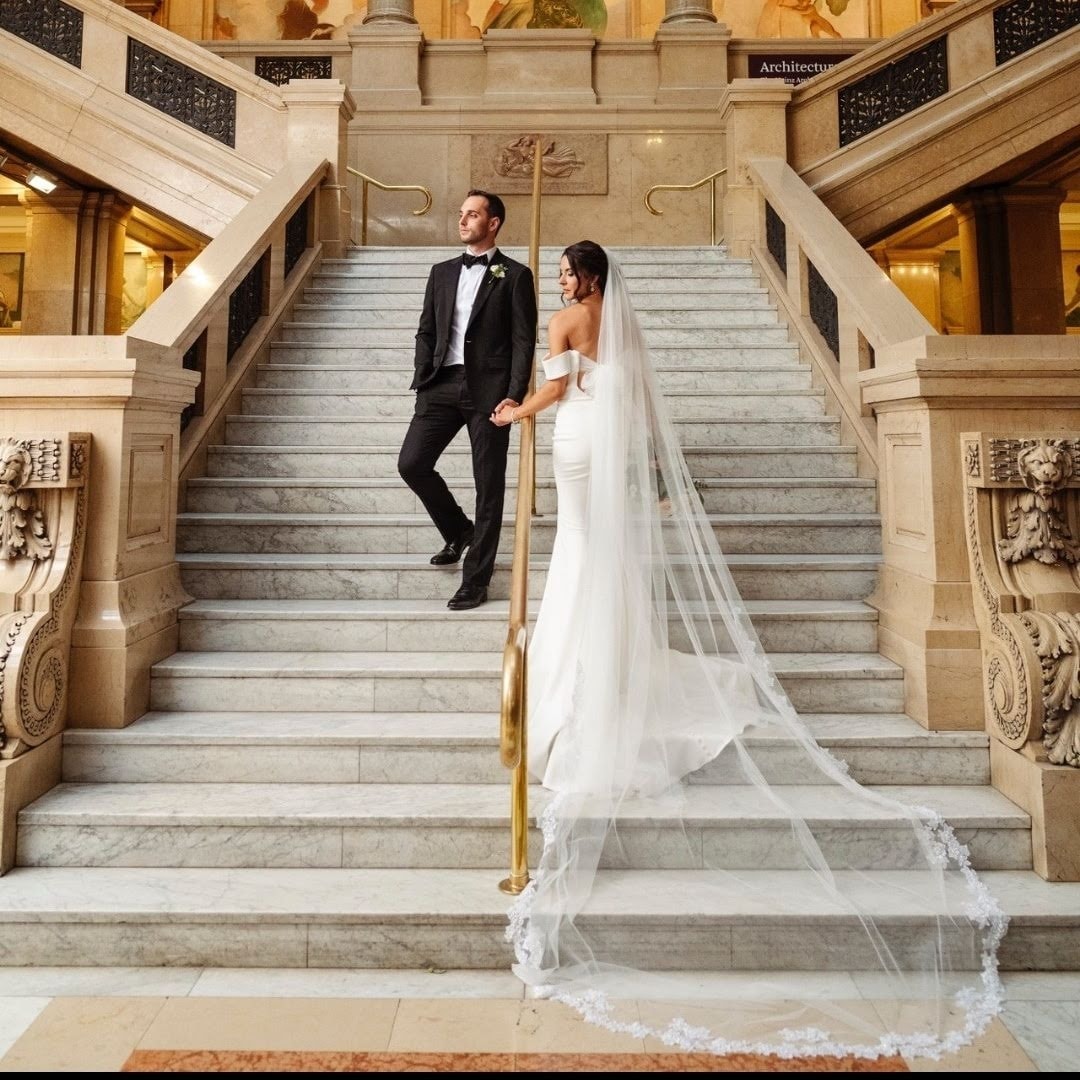 Bride and groom on grand marble staircase with cathedral veil