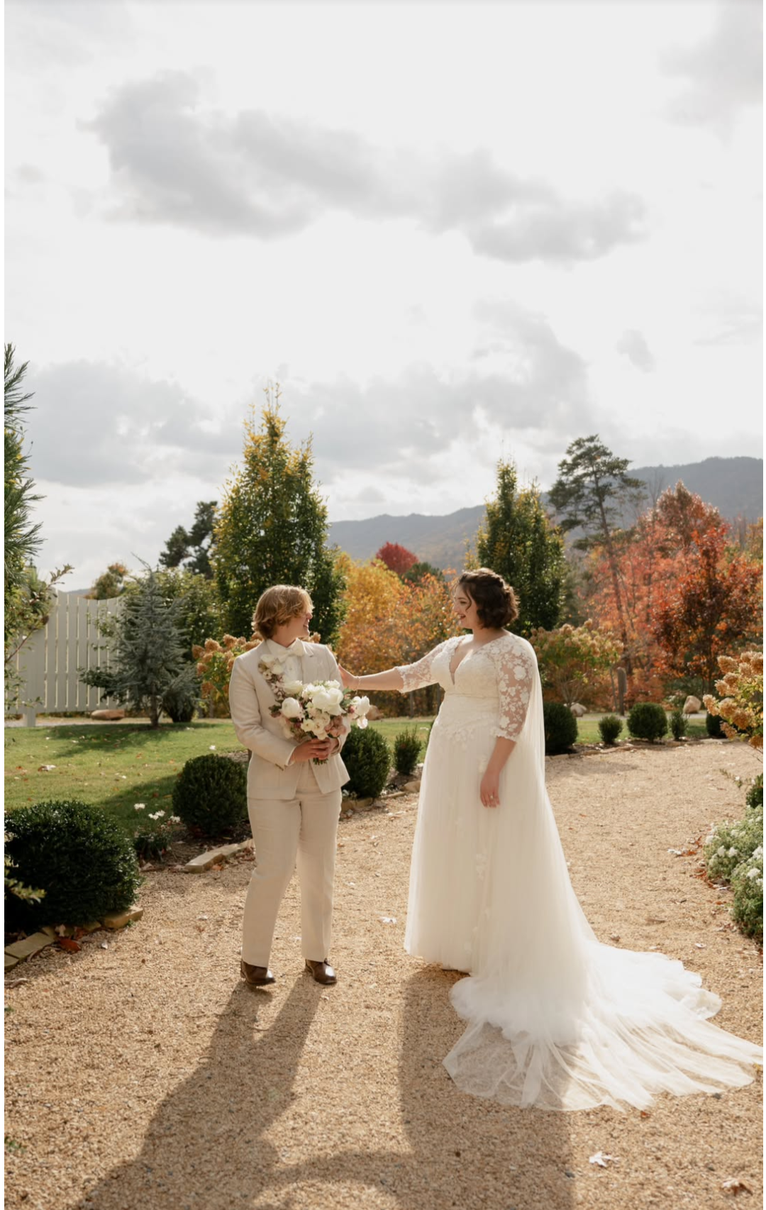 Two brides in autumn garden first look with lace cape gown