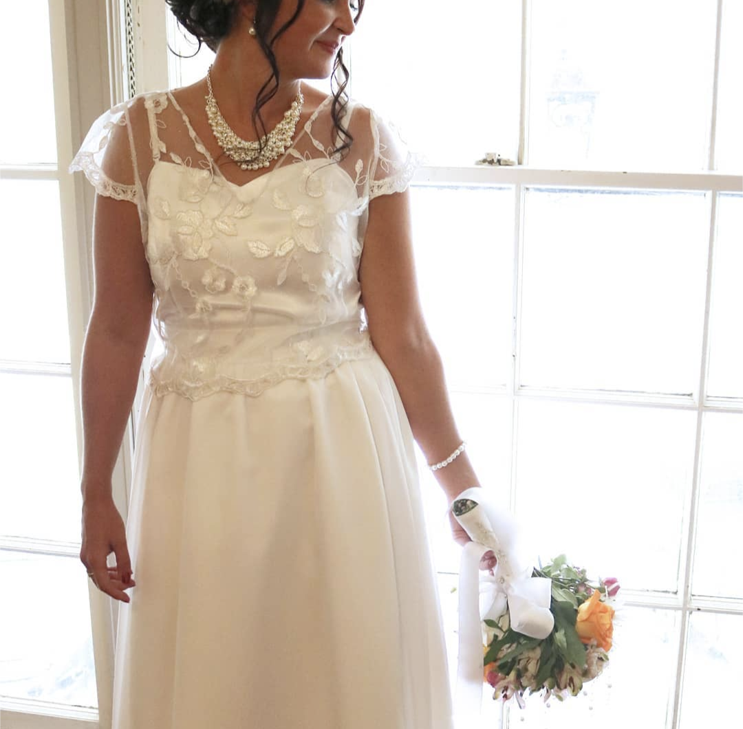 Bride in vintage-style lace gown holding colorful bouquet by window