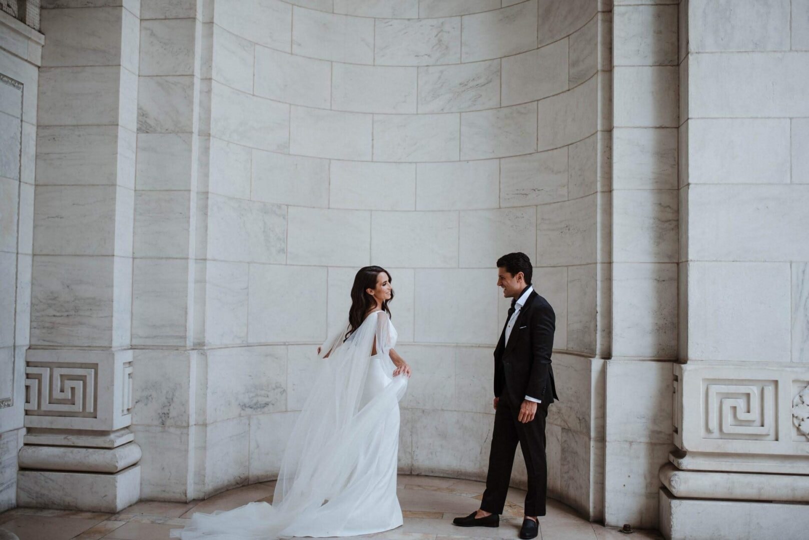 Bride in flowing cape gown with groom in marble rotunda